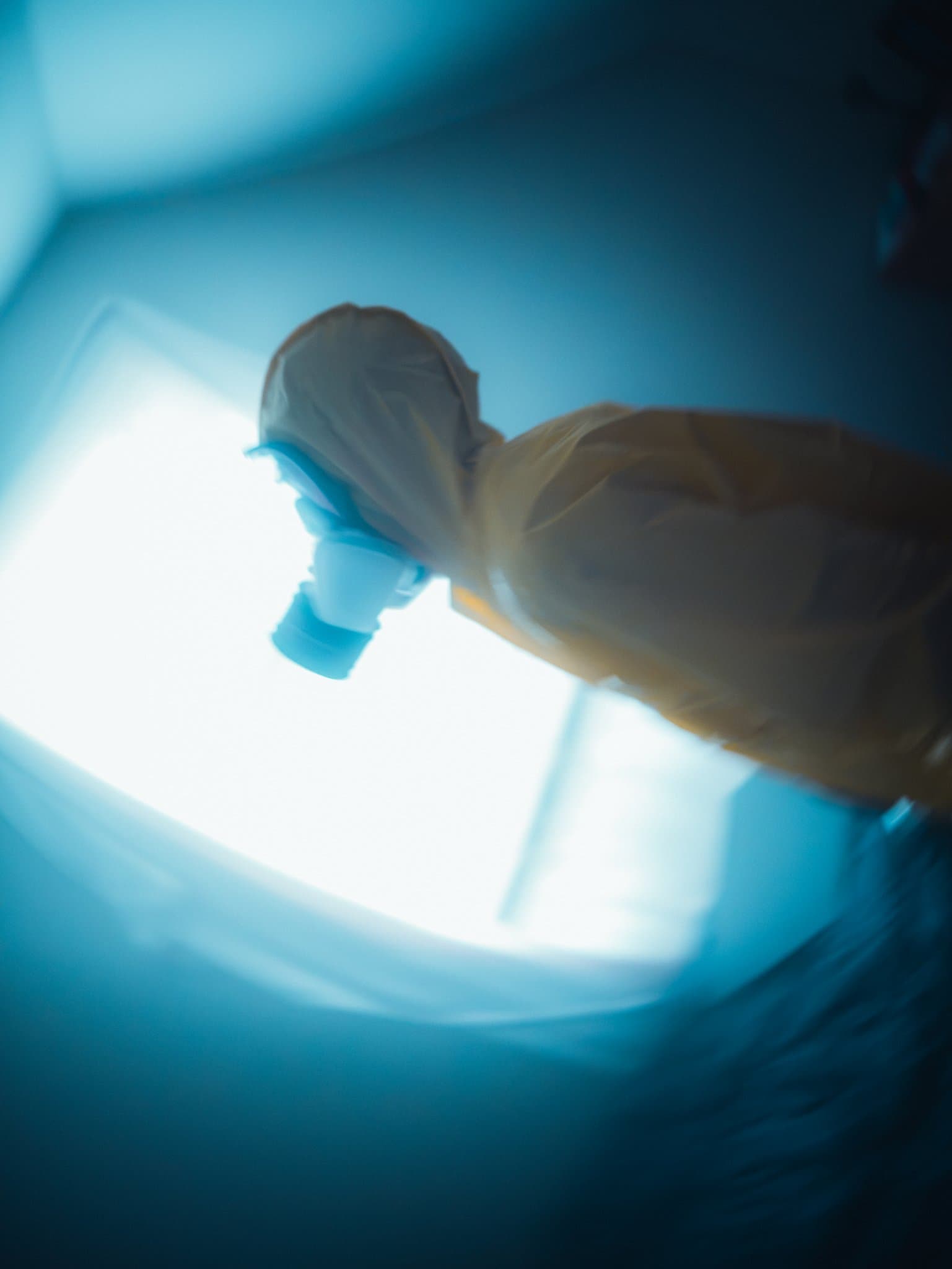 Motion-blurred figure in a hazmat suit and gas mask at a tilted angle, streaking past a blown-out bright window — human-made reference photo on Slow Sync